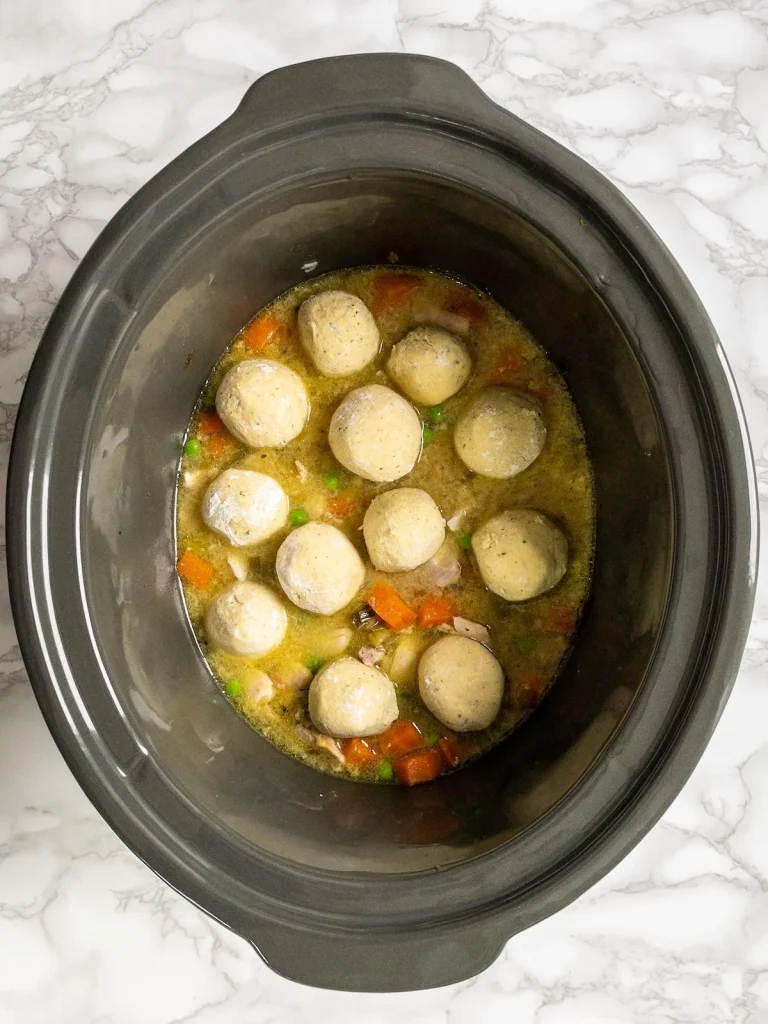 Dumplings placed on top of the chicken mixture in the slow cooker