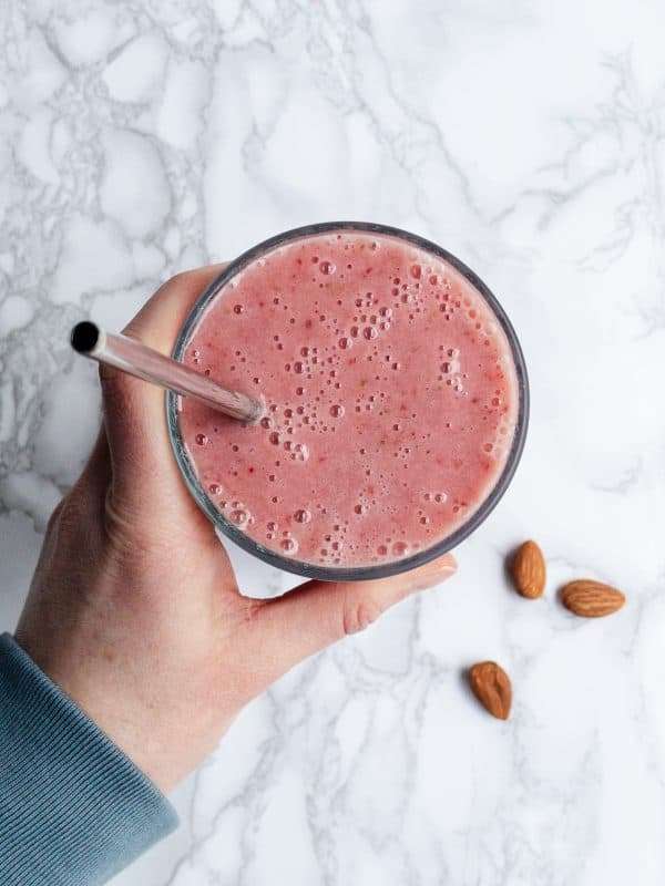 Hand holding a tall glass of Strawberry Smoothie Without Yogurt