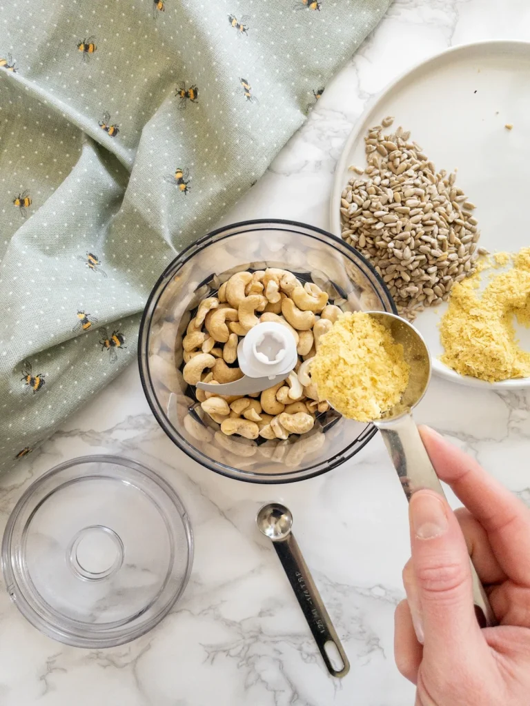 Adding the vegan parmesan cheese ingredients to a small food processor for blending.