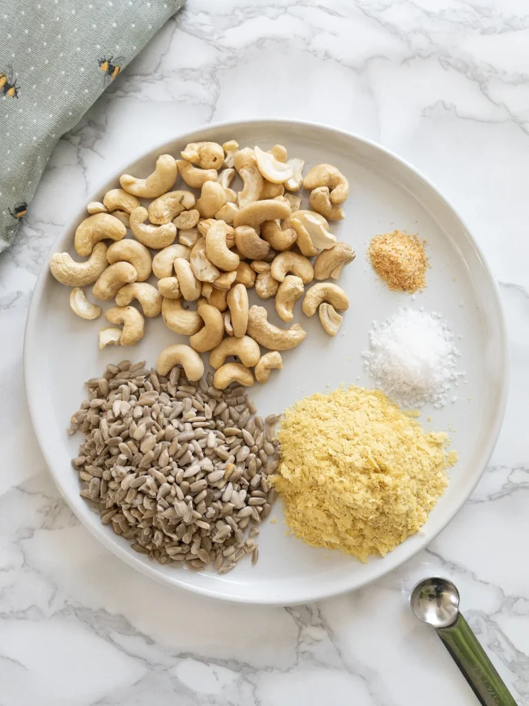 Homemade dairy free parmesan ingredients on a plate: cashews, sunflower seeds, nutritional yeast, garlic powder and salt.