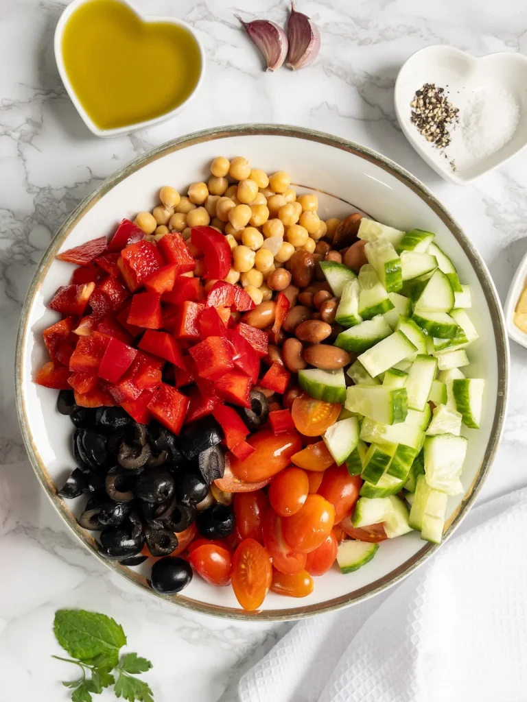 Chickpeas, borlotti beans, cannellini beans, cucumber, olives and tomatoes for vegan bean salad. Next, add the red pepper.