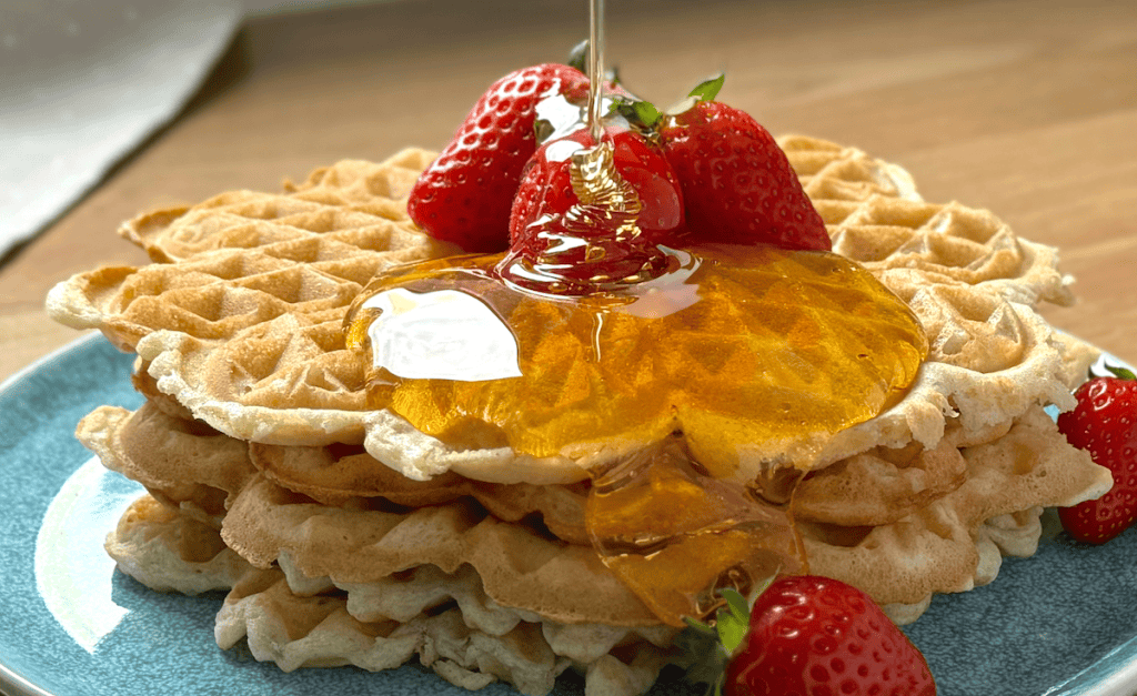 Stack of waffles on a plate with syrup and strawberries