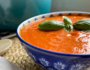 Blue bowl of dairy free tomato soup with basil garnish on the top