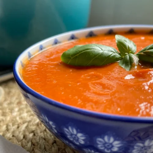 Blue bowl of dairy free tomato soup with basil garnish on the top