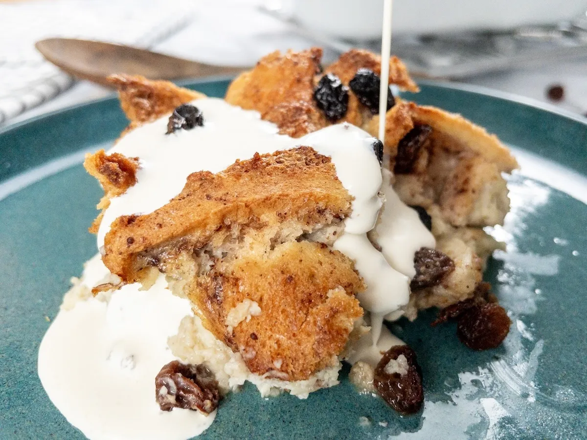 Homemade dairy-free bread pudding served on a plate and topped with plant-based cream.