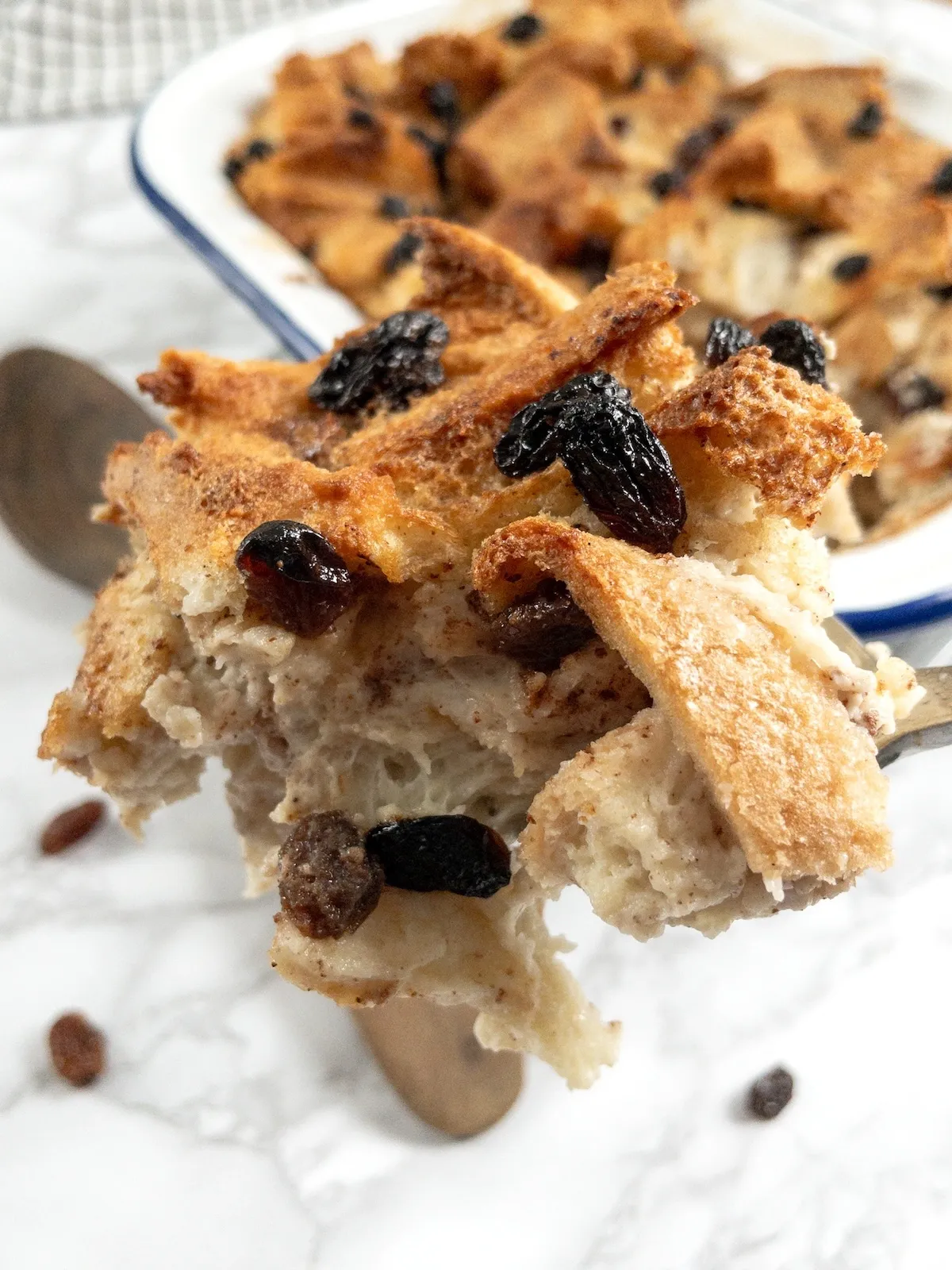 A large spoonful of fairy-free bread and butter pudding with golden crust and raisins, served warm.