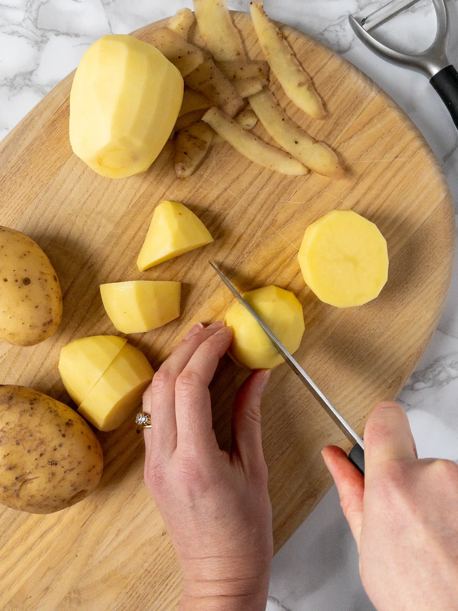 Hands chopping potatoes on a cutting board.