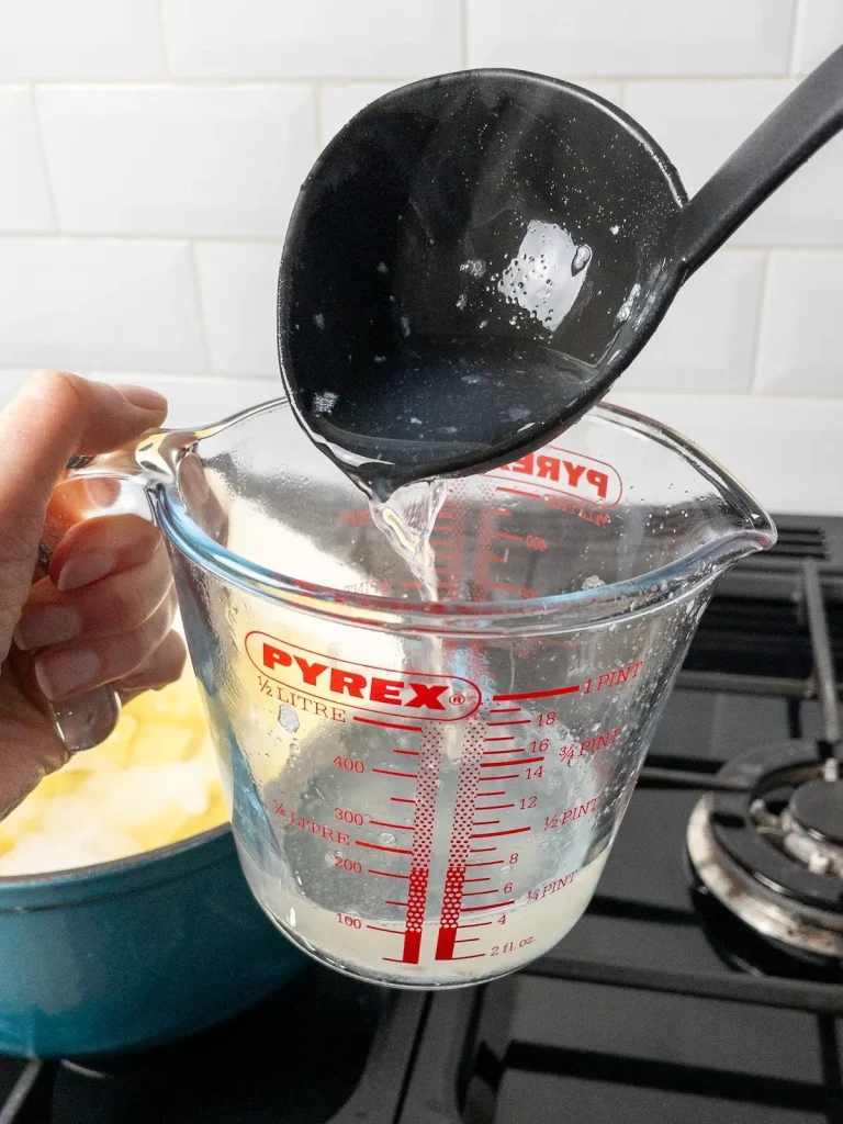 A ladleful of potato cooking water is poured into a jug.