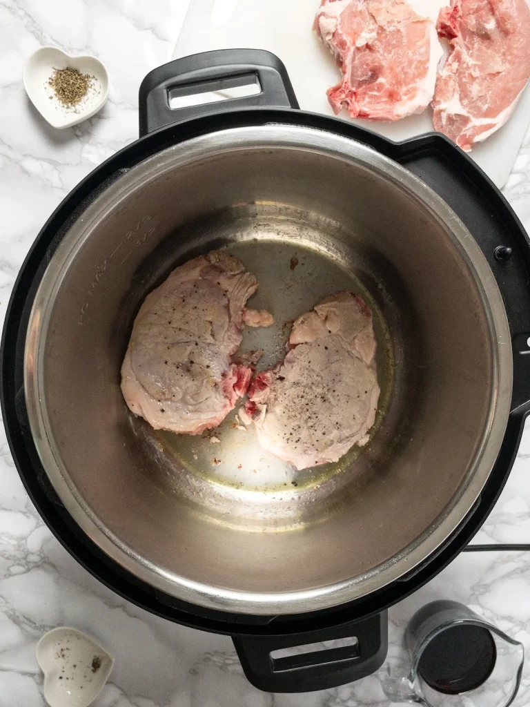 Searing frozen pork chops in the Instant Pot before pressure cooking.