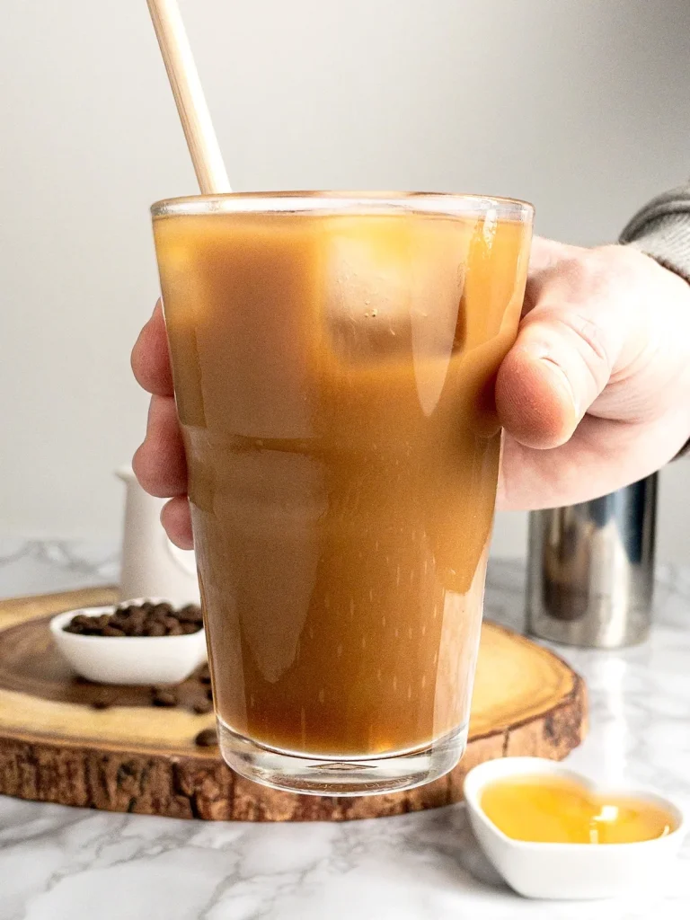 Iced coffee with almond milk and honey in a clear cup with a straw.