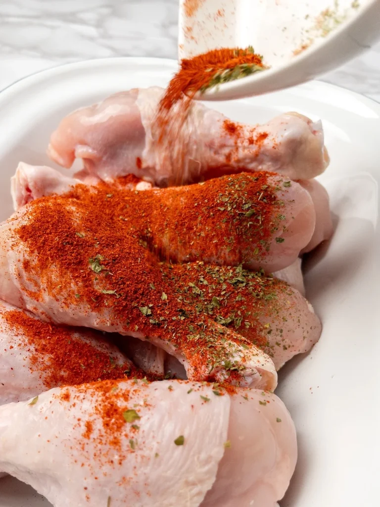 Seasoning drumsticks before frying in a skillet.