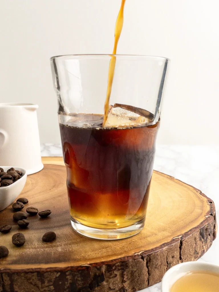 Pouring cold brew coffee into a tall glass with ice.