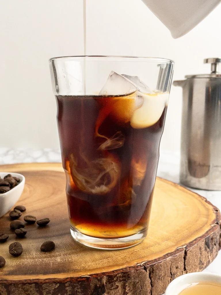 Pouring almond milk into cold brew coffee with a honey syrup, perfect morning coffee.