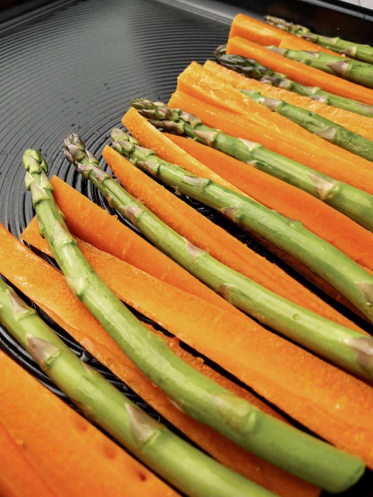 Sliced carrots and asparagus prepared on a baking tray before roasting.