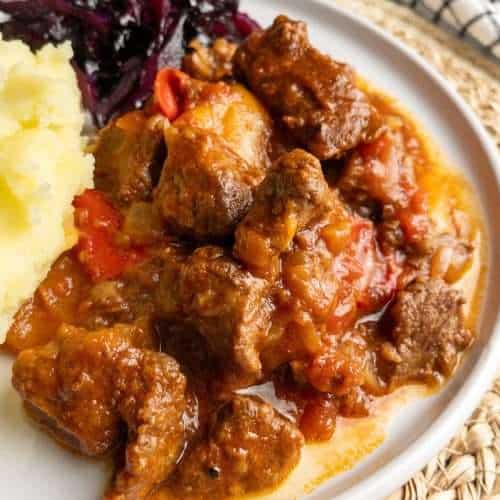 A plate of goulash serve with potato and braised red cabbage.