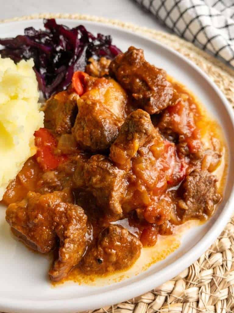 A plate of goulash serve with potato and braised red cabbage.