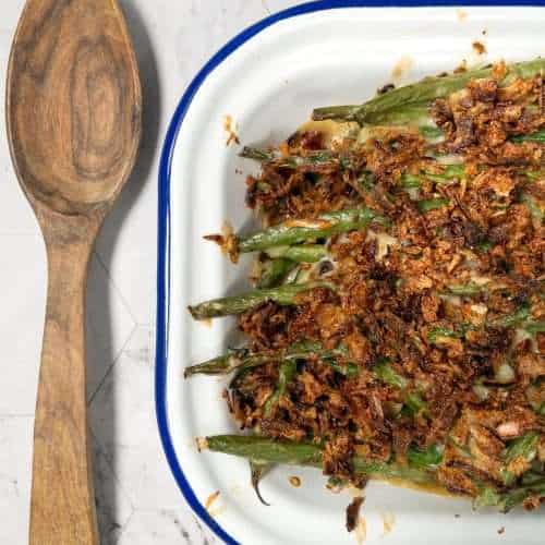 Baked dairy-free green bean casserole in a dish next to a wooden spoon.