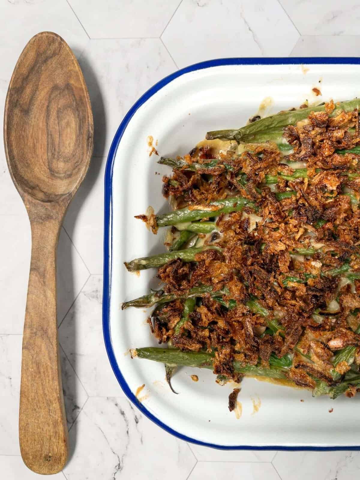 Baked dairy-free green bean casserole in a dish next to a wooden spoon.