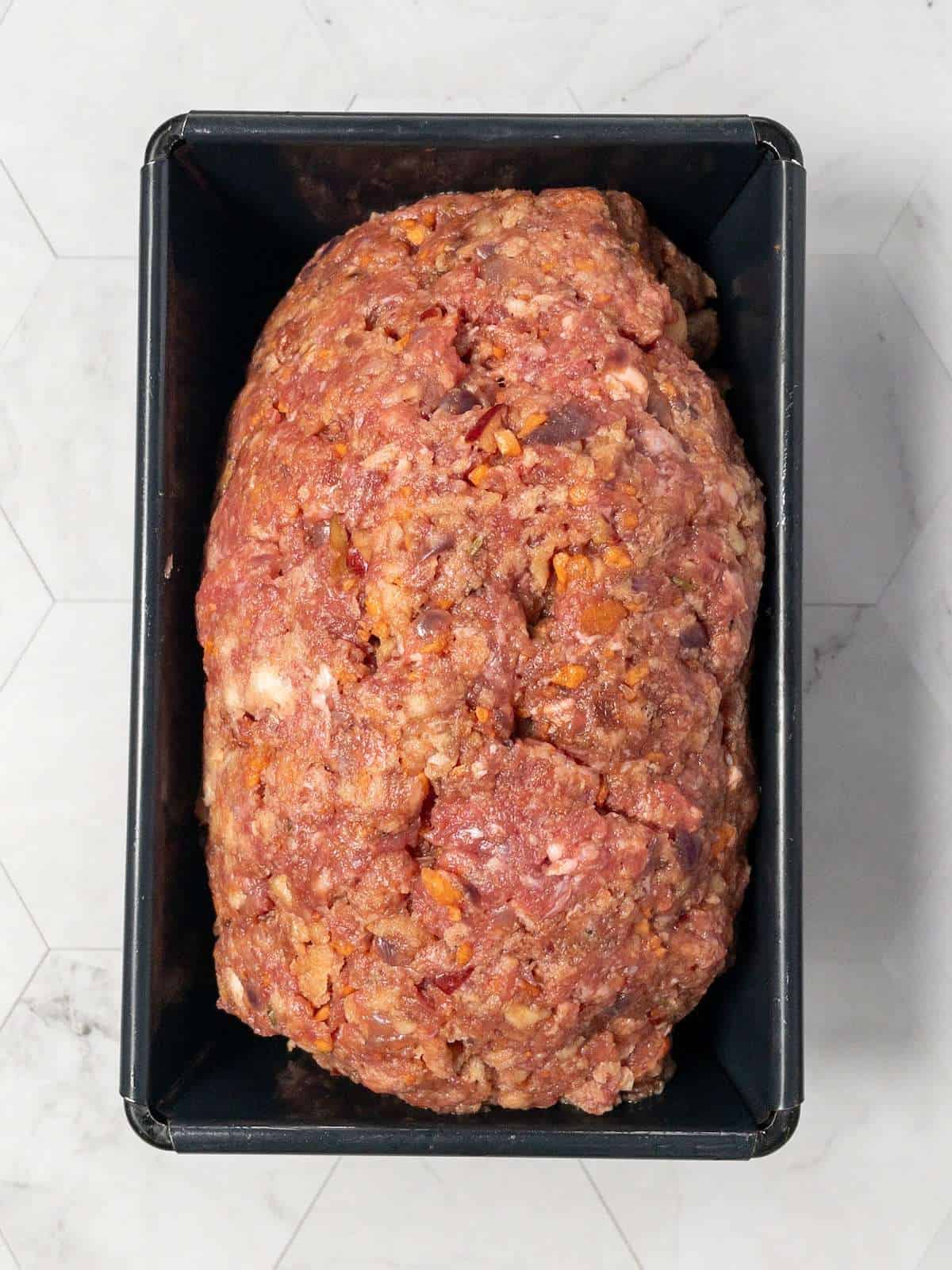 Uncooked meatloaf in a loaf tin, shaped and ready to bake.