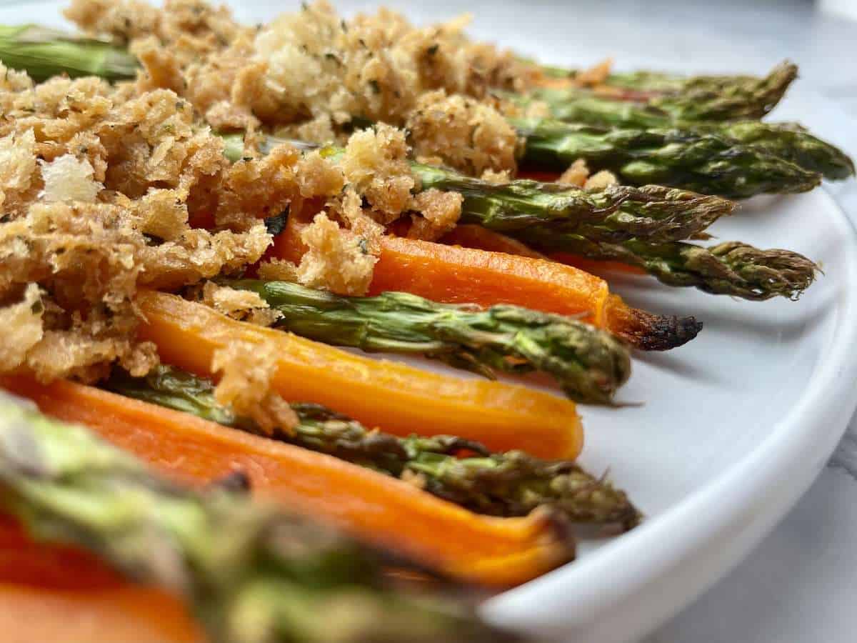 Close-up of roasted carrots and asparagus with crispy breadcrumb topping.