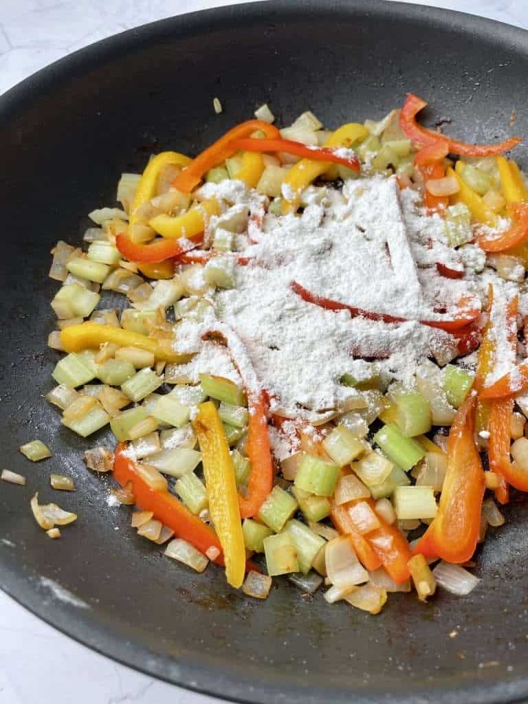 Adding flour to the vegetable mixture for Cajun smothered chicken.