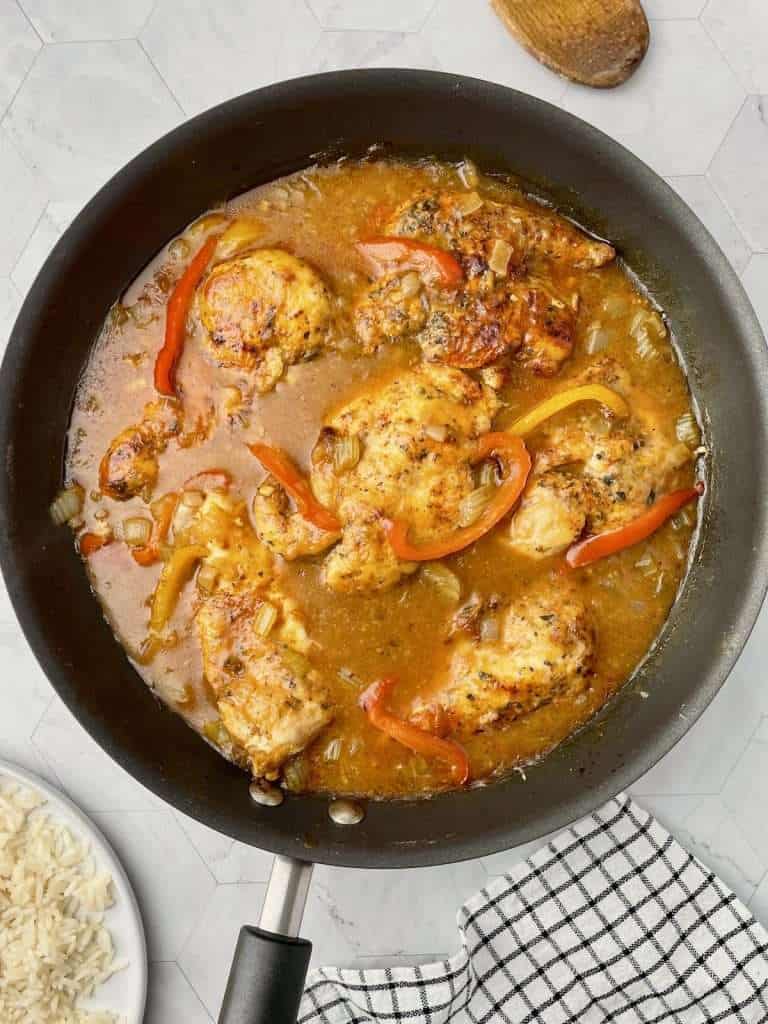 Cajun chicken cooking in a skillet with rich gravy.